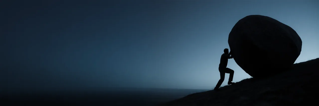 A lone figure in silhouette pushing a large boulder up a steep slope above the sea at dusk